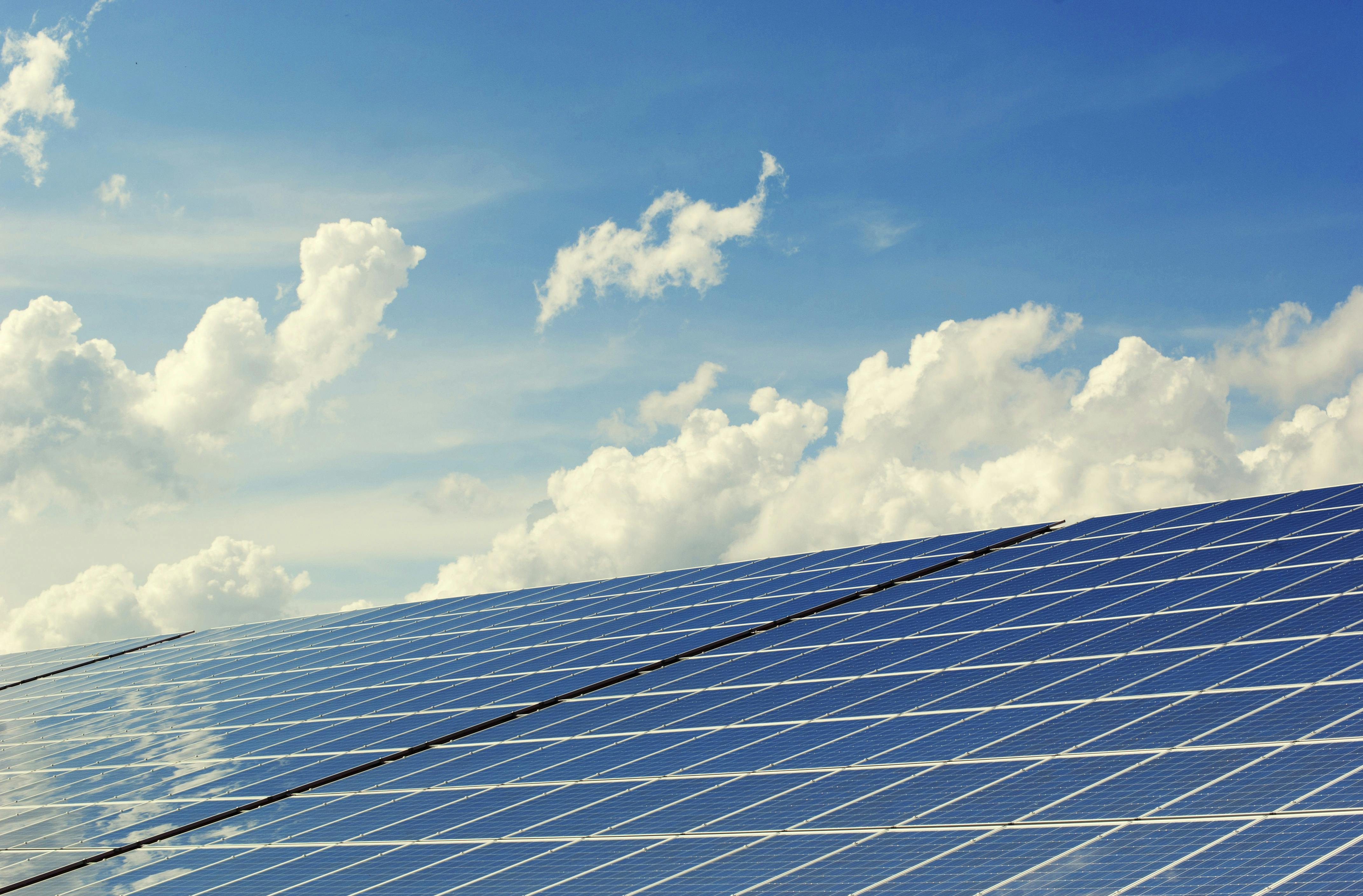 Blue solar panels with blue sky and clouds in background