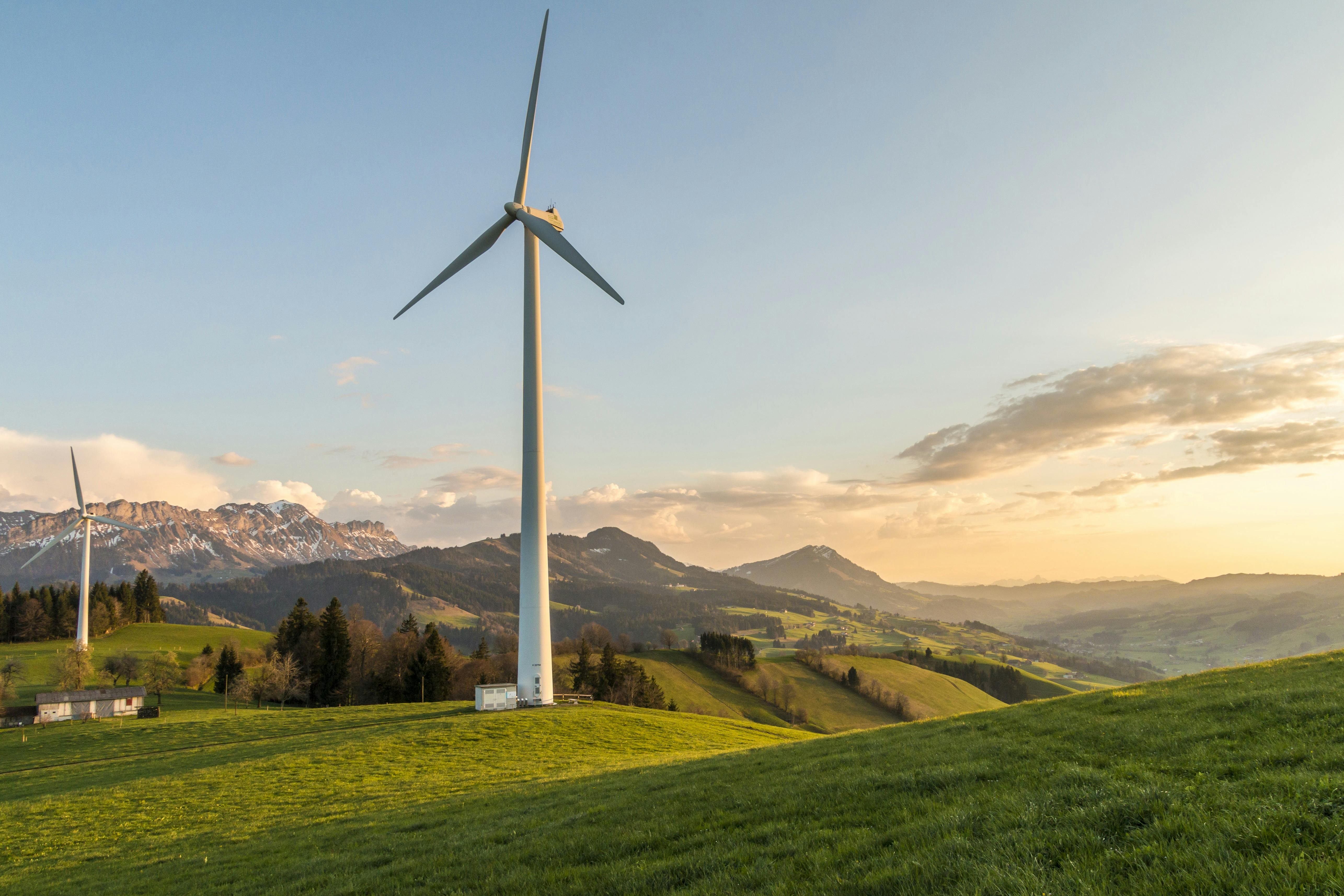 Wind turbine on top of grassy hill with other turbine and mountains in background